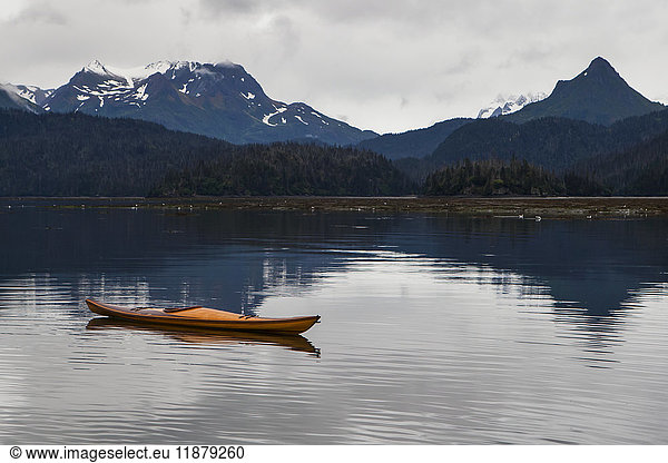 'A kayak sits on the tranquil water with a view of forests and a mountain range in the background  Kachemak Bay State Park; Alaska  United States of America'