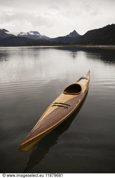 'A wooden kayak sits on tranquil water with a view of the mountains in the background  Kachemak Bay State Park; Alaska  United States of America'
