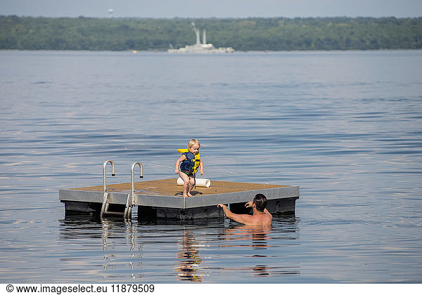'A young Caucasian girl prepares to jump off a floating dock into her dad's arms in Seneca Lake in upstate New York  the naval barge  no longer in service  is in the background; Dresden  New York  United States of America'