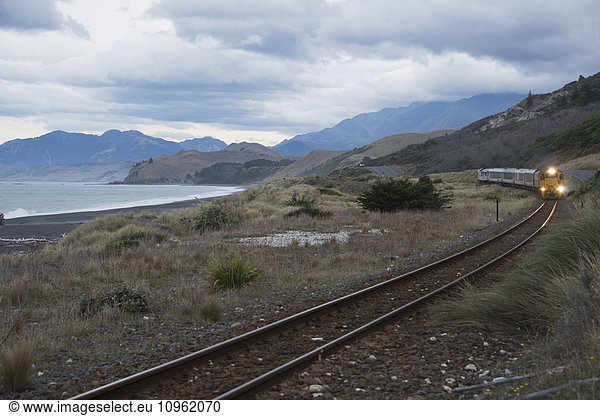 'Approaching train with scenic sea and mountain backdrop on East coast of New Zealand's South Island; New Zealand'