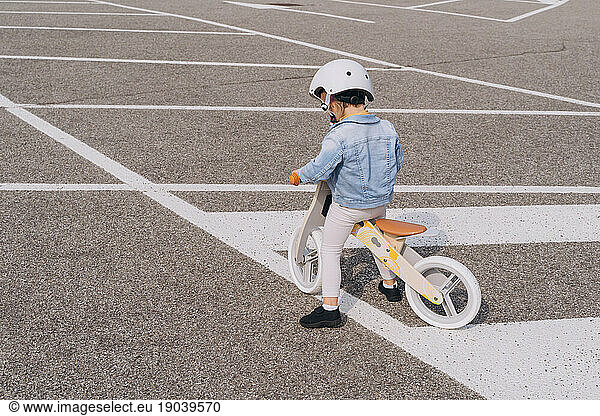 Ð¡aucasian girl preschooler riding wooden balance bike on asphalt road