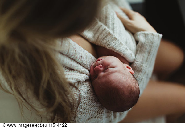 Über-Schulter-Ansicht einer mittelgroßen erwachsenen Frau  die ihre neugeborene Tochter in eine Strickjacke gewickelt wiegt