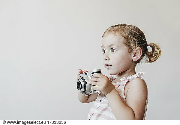 Überraschtes Mädchen mit Spielzeugkamera vor weißem Hintergrund