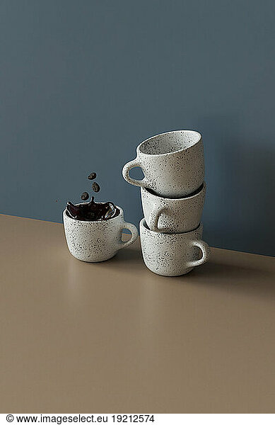 3D render of coffee beans falling into mug of coffee standing by stack of empty mugs