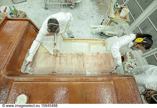 3dis Personen tragen in einer Bootsbaufabrik Fiberglas auf eine Form auf