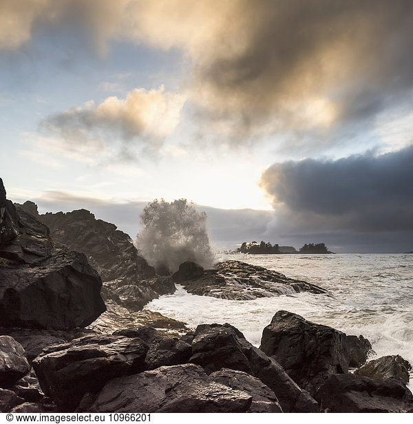 'Glowing clouds at sunset with waves crashing against the rocks; Tofino British Columbia Canada'