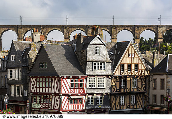 'Half timbered old buildings with large stone viaduct in the background with blue sky and clouds; Morlaix  Brittany  France'