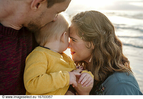 30 Jahre alte Eltern kuscheln liebevoll mit ihrem 6 Monate alten Baby am Meer