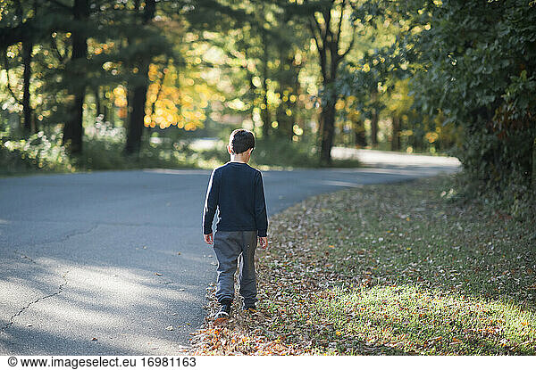 8-10 Jahre alter Junge  der im Herbst eine von Bäumen gesäumte Straße hinunterläuft