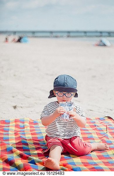 . 2 Jahre alter Junge trinkt Saft am Strand.