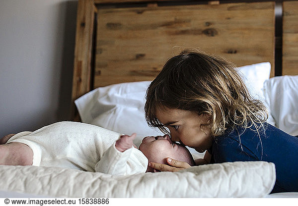 4 Jahre alter küssender Kopf einer neugeborenen Schwester auf Bett mit Kissen