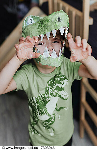 5 Jahre Junge spielt in seinem Zimmer  trägt grünes T-Shirt mit Dinosaurier-Aufdruck und T-Rex-Maske
