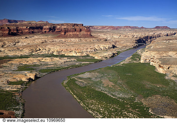 'Low altitude aerial view of the Colorado River winding through canyon country of southern Utah  a bridge spanning the river in the background with red rock canyon walls and blue skies; Utah  United States of America'