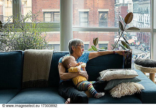 Ältere Frau hält ihre kleine Enkelin und trinkt aus einer Babyflasche