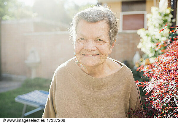 Ältere Frau lächelt in der Nähe der Pflanze im Hinterhof