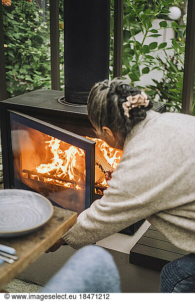 Ältere Frau legt während einer Dinnerparty Brennholz in den Kamin