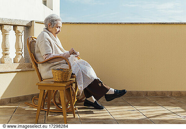 Ältere Frau näht mit Nadel und Faden auf einer Außenterrasse