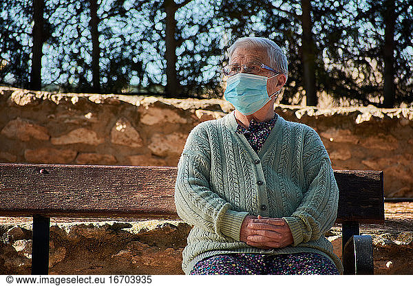 Ältere Frau sitzt mit Maske auf einer Parkbank