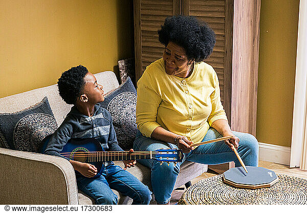 Ältere Frau spielt Schlagzeug  während ihr Enkel zu Hause Gitarre spielt