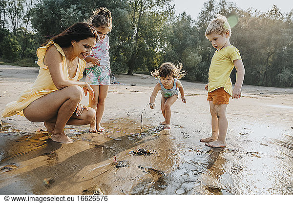 Ältere Frau und Kinder entdecken Krabben am Strand