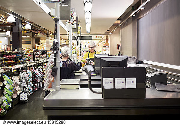 Ältere weibliche Kassiererin hilft Kunden an der Supermarktkasse