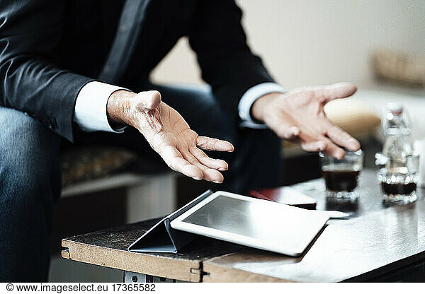 Älterer Geschäftsmann sitzt mit digitalem Tablet und gestikuliert  während er in einem Café sitzt