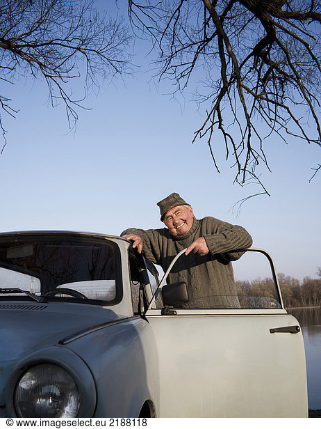Älterer Mann beim Auto am Flussufer  lächelnd  Porträt