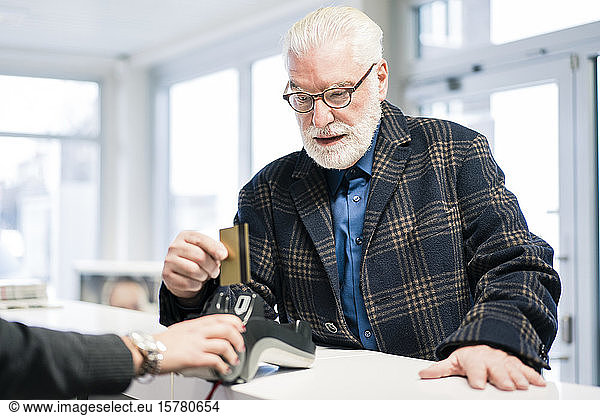 Älterer Mann bezahlt mit Kreditkarte an der Ladentheke eines Geschäfts