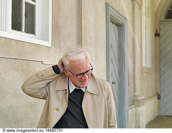 Älterer Mann im Regenmantel  der sich am Kopf kratzt  Kopenhagen  Hovedstaden  Dänemark