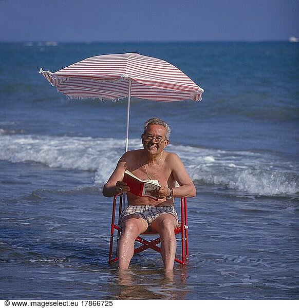Älterer Mann im Sonnenstuhl und Sonnenschirm im Meer  Strand und Wellen  Older man in the solar chair and sunshade in the sea  beach and waves