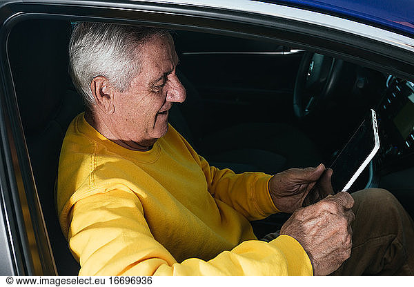Älterer Mann lächelt beim Segeln auf einem Tablet in einem Fahrzeug