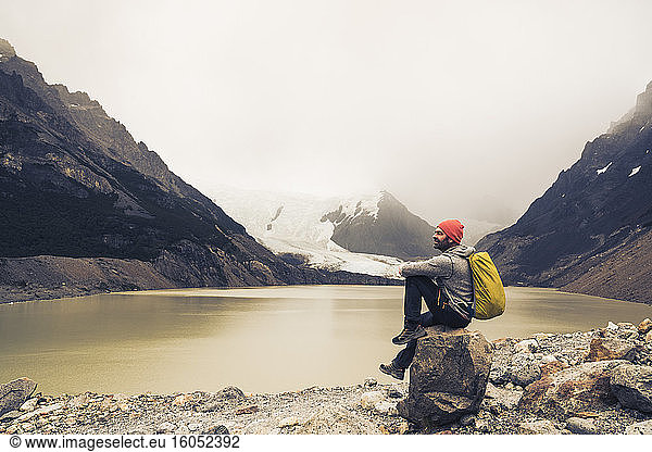 Älterer Mann mit Rucksack sitzt auf einem Felsen am See in Patagonien  Argentinien