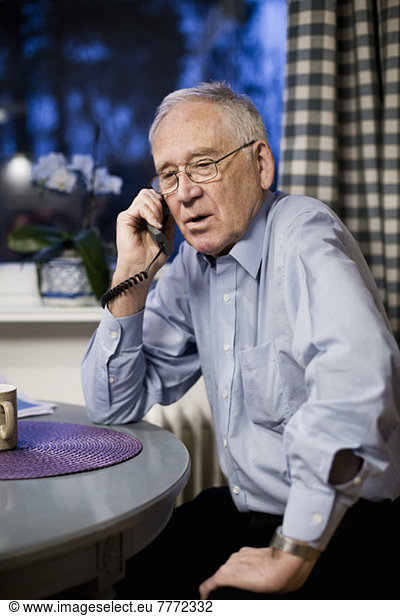 Älterer Mann mit Telefon am Tisch