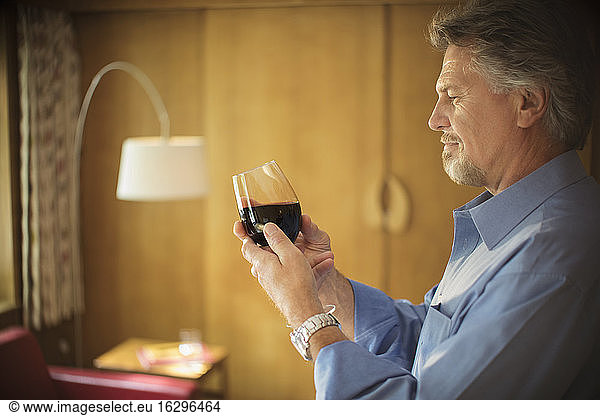 Älterer Mann probiert Rotwein im Wohnzimmer
