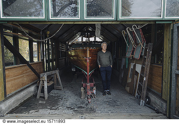 Älterer Mann steht an einem Holzboot in einem Bootshaus