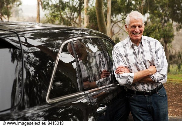 Älterer Mann steht gegen schwarzes Fahrzeug