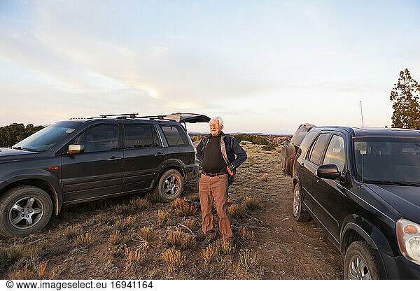 Älterer Mann steht zwischen SUV-Autos bei Sonnenuntergang  Galisteo Basin
