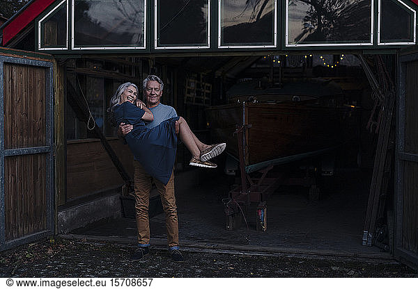 Älterer Mann trägt seine Frau vor dem Bootshaus