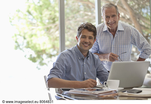 Älterer Mann und jüngerer Mann lächeln zusammen am Schreibtisch