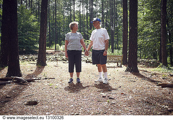 Älteres Ehepaar hält im Wald Händchen und steht dabei im Wald