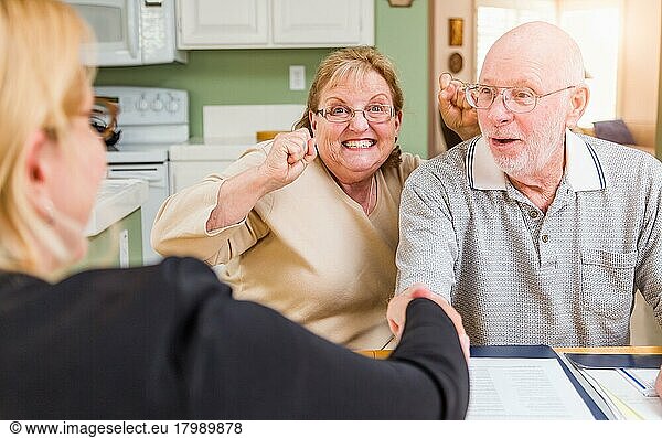Älteres erwachsenes Paar  das mit einem Agenten bei der Unterzeichnung von Dokumenten in seiner Wohnung feiert