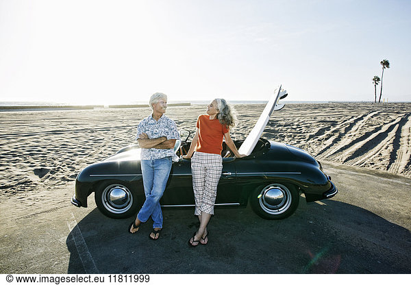 Älteres kaukasisches Paar lehnt an Cabrio mit Surfbrett am Strand