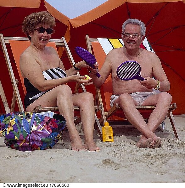 Älteres Paar am Strand im Sonnenstuhl  mit Ball und Schläger  Fitness  Bewegung  Older pair on the beach in the solar chair  with ball and racquet  fitness  movement