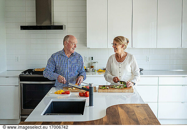 Älteres Paar unterhält sich beim Gemüseschneiden auf der Kücheninsel zu Hause