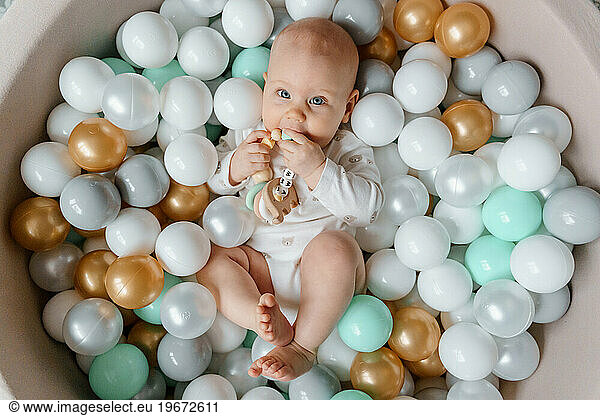 6 month old baby lies in the pool with balls and gnaws teether