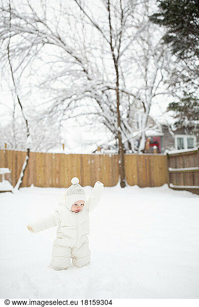 12-month-old Caucasian baby boy in snow suit throws snow in air.