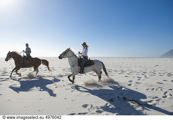 2 people riding horses in the sand