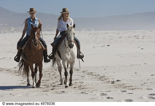 2 people riding horses on the beach