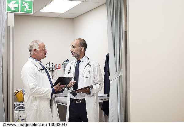 Ärzte diskutieren medizinische Berichte  während sie im medizinischen Untersuchungsraum stehen
