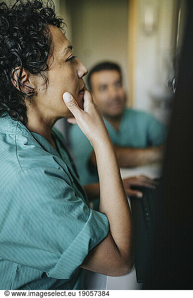 Ärztin mit Hand am Kinn bei der Arbeit am Computer im Krankenhaus